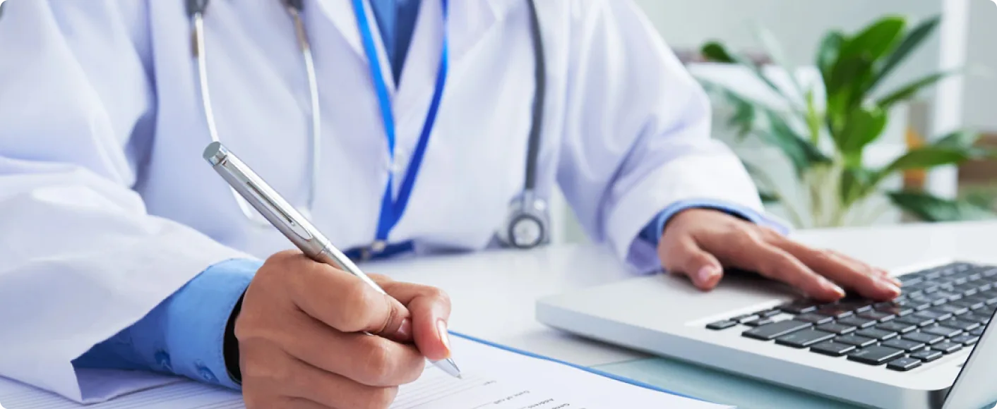 Physician completing a patient form beside a laptop